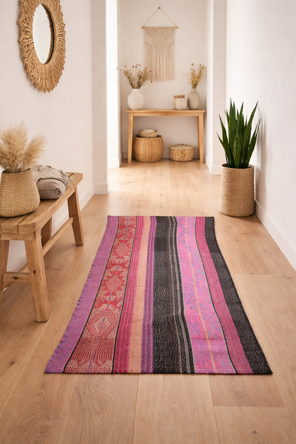 Minimalistischer Flur im Boho-Stil mit hellem Holzboden. Ein asymmetrischer Frazada-Runner in Pink, Violett und Schwarz liegt zentral. Holzbank, Pflanze und dezente Deko sorgen für Ruhe. Weiches Tageslicht unterstreicht die natürliche Stimmung.