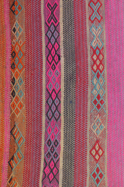 Lichtdurchfluteter Boho-Flur mit warmem Holzboden. Ein peruanischer Frazada-Teppich in Rosa- und Orangetönen mit leichten Asymmetrien liegt mittig. Holzbank, Pflanze und schlichte Deko ergänzen den Raum. Natürliches Licht wirkt weich und harmonisch.