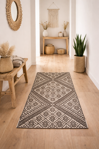 Heller, minimalistischer Flur im Boho-Stil mit hellem Holzboden. Ein schwarz-cremefarbener peruanischer Frazada-Teppich mit geometrischem Muster liegt mittig. Holzbank, Pflanze, Keramik und Makramee ergänzen den Raum. Natürliches Licht schafft eine warme, ruhige Atmosphäre.